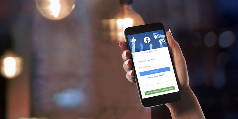 Personne tenant son téléphone portable ouvert sur une page Facebook