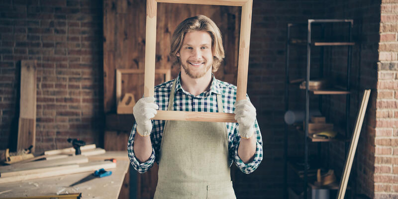 Artisan souriant se mettant en scène dans un cadre en bois