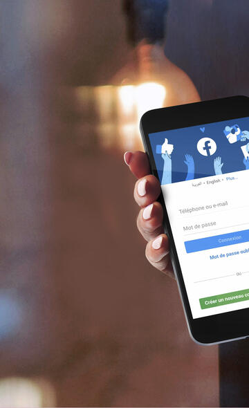 Personne tenant son téléphone portable ouvert sur une page Facebook