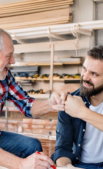 Un artisan souriant complice avec l'artisan à qui il transmet son entreprise 