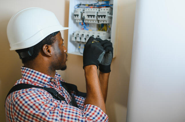 Jeune artisan électricien intervenant sur un tableau électrique
