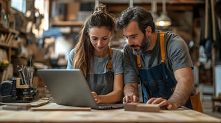 Deux artisans regardent leur ordinateur portable dans leur atelier de menuiserie