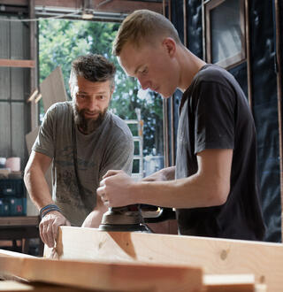 Apprenti charpentier ponçant une plache avec son maître d'apprentissage