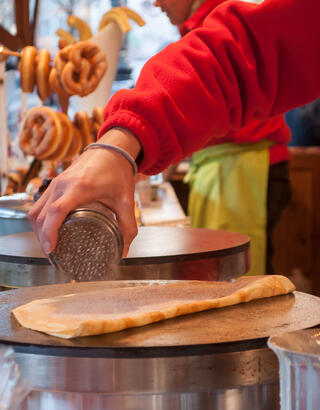 Artisan crêpier sucrant une pâte à crêpe