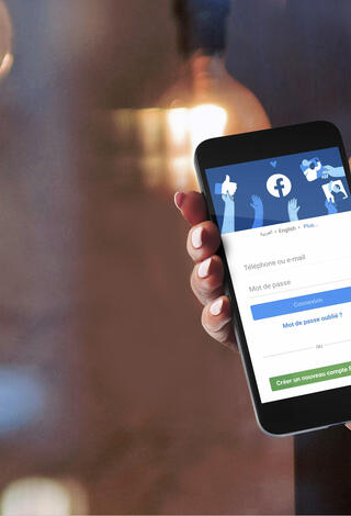 Personne tenant son téléphone portable ouvert sur une page Facebook